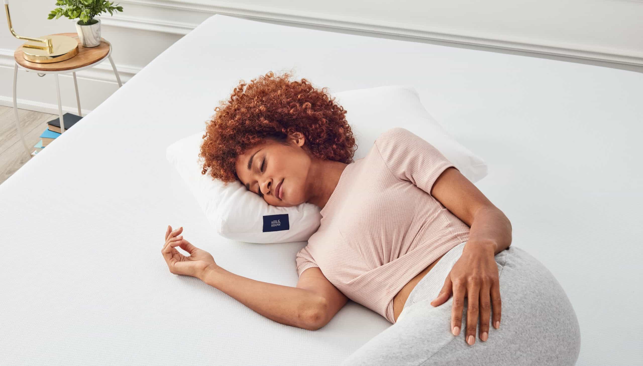 Woman sleeping on her side on top of a white mattress and pillow.