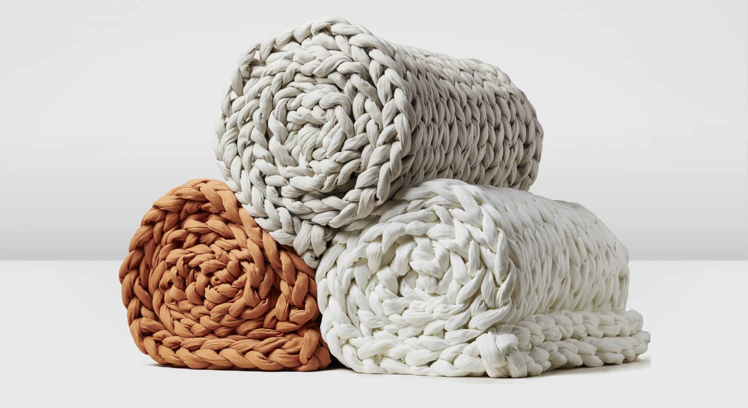 Three rolled up hand-knit weighted blankets stacked on top of one another pyramid-style.