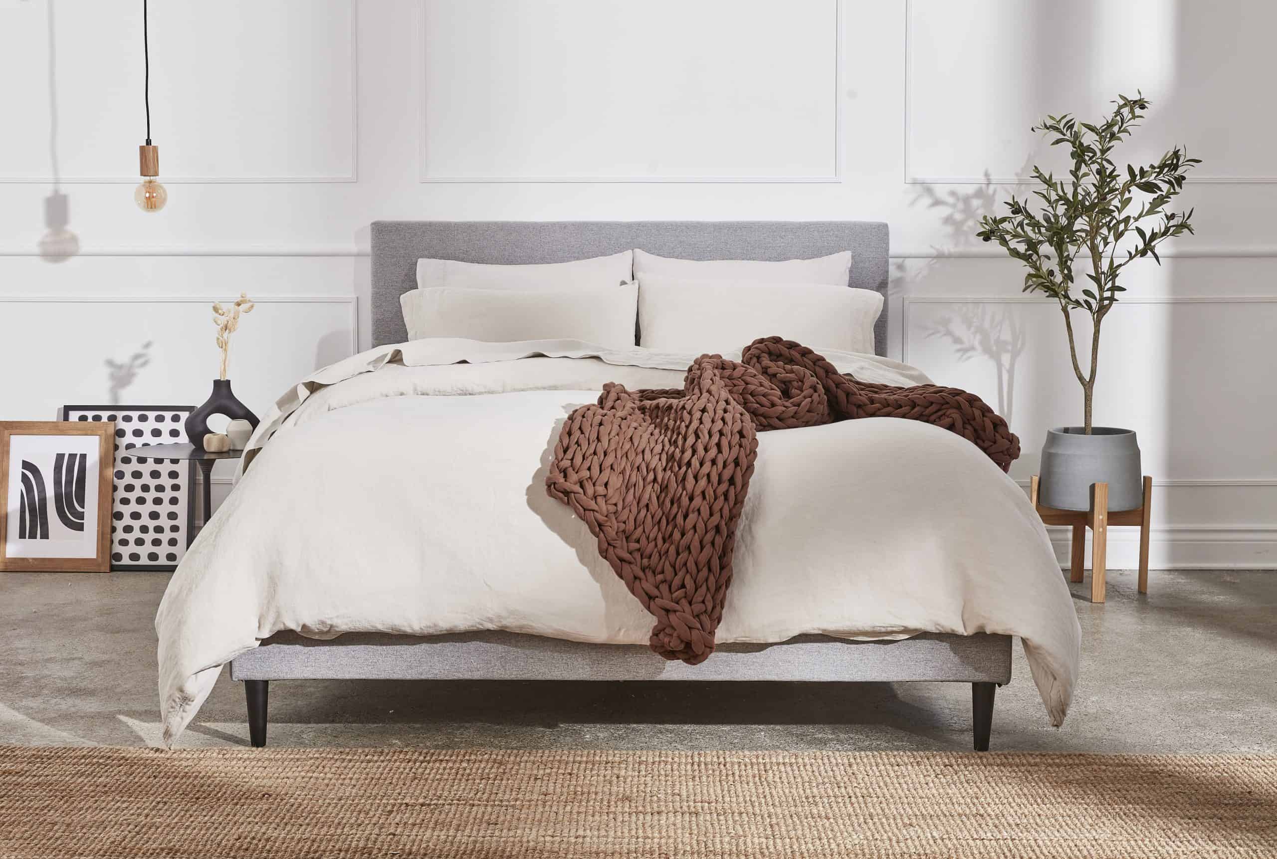 A brown weighted blanket drapes over a made bed in white bed sheets.